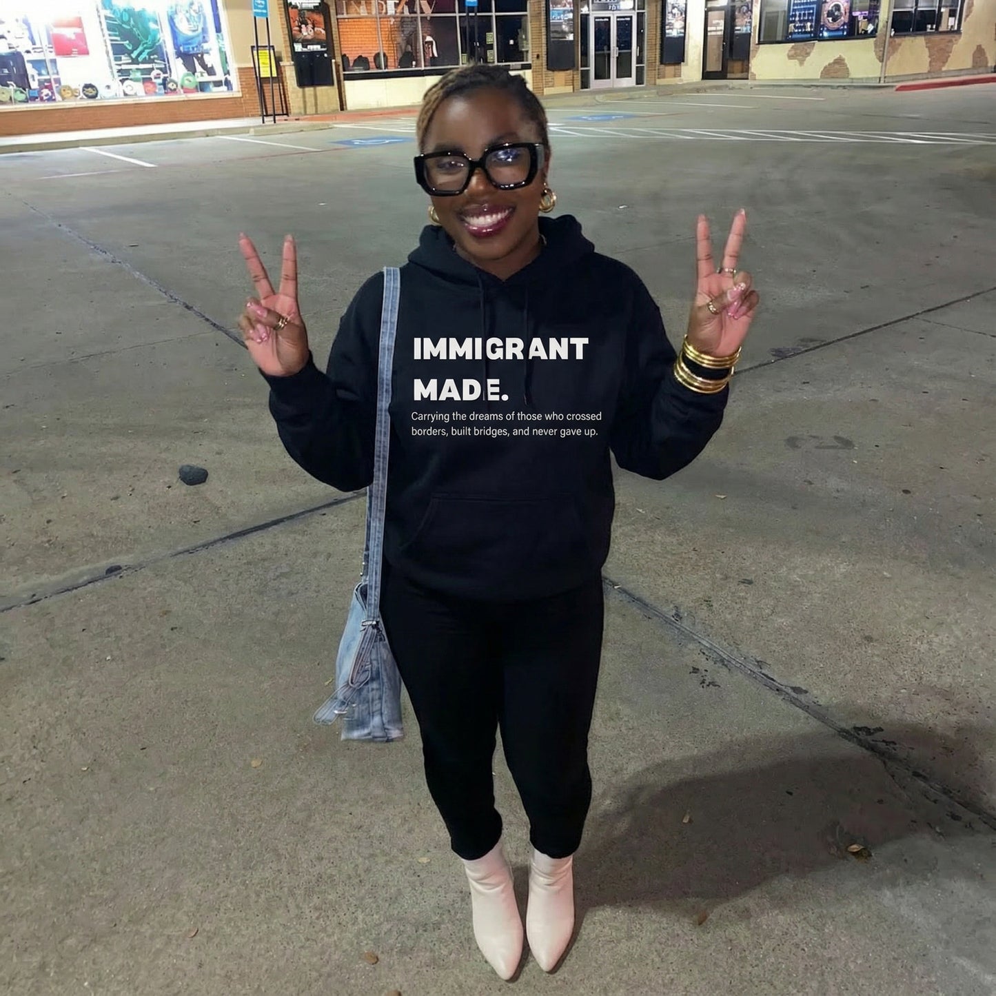Person wearing a black hoodie with 'IMMIGRANT MADE' text, standing on a street.